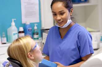 [Featured Image] A dental assistant speaks with a patient in the dentist's office.