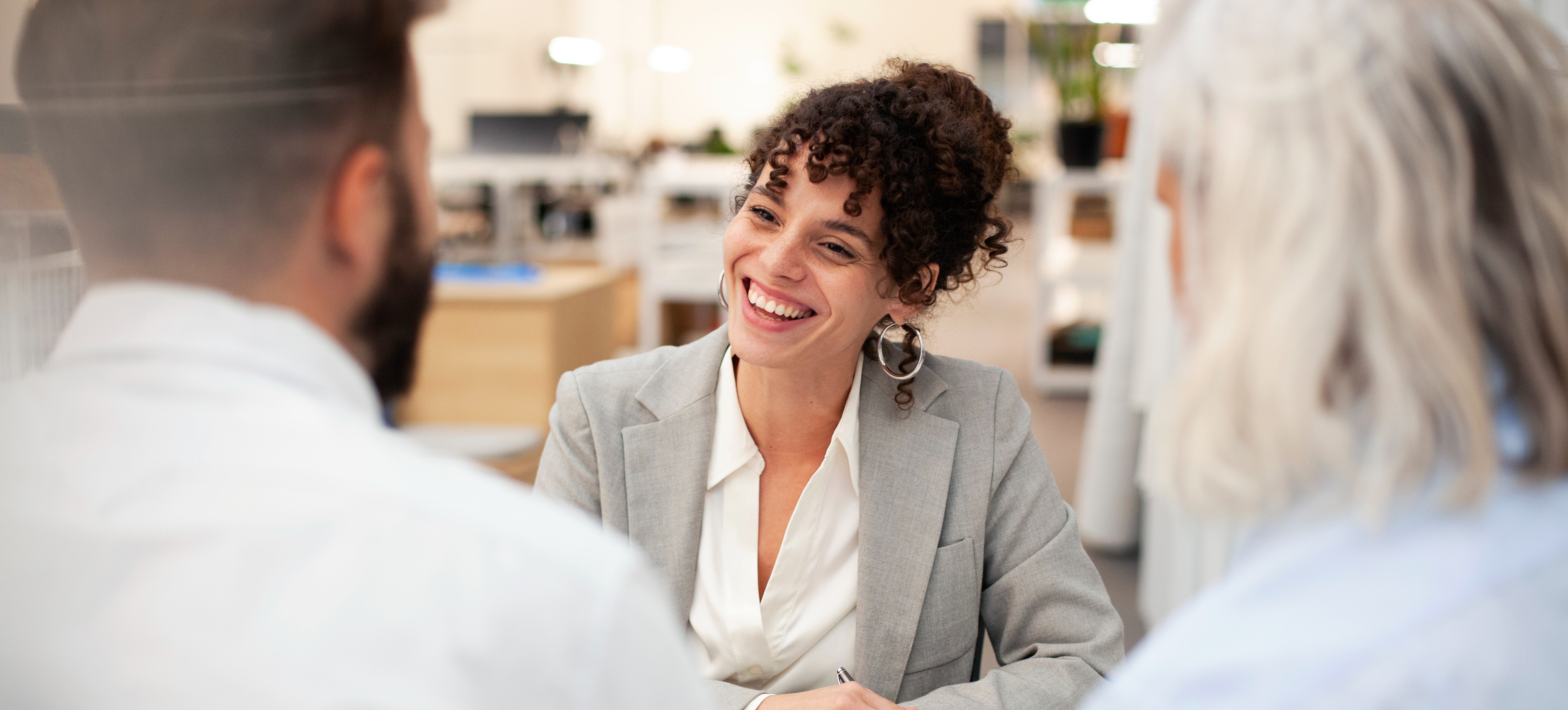 [Featured Image] A smiling financial advisor, one of many possible economics jobs, talks to two clients across a desk.
