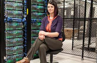 [Featured image] A data server engineer sits on a rolling chair in front of a wall of computer servers.