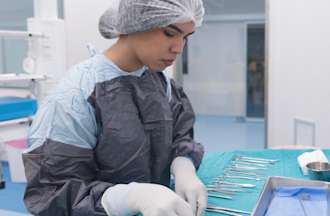 [Featured Image] A surgical technologist wearing scrubs organizes a tray of tools in an operating room.