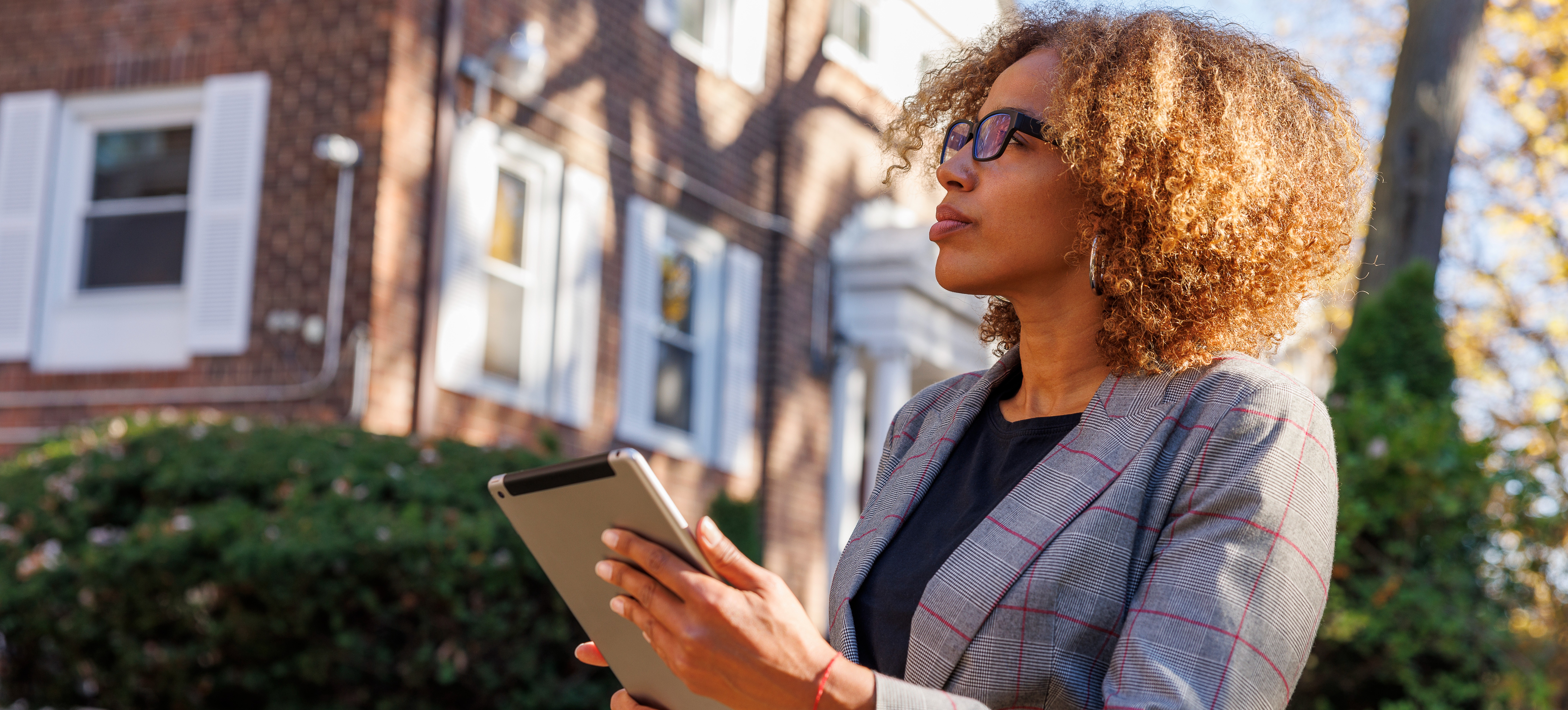 [Featured Image] A female real estate appraiser with a tablet is in a neighborhood gathering competitive intelligence for a business meeting.
