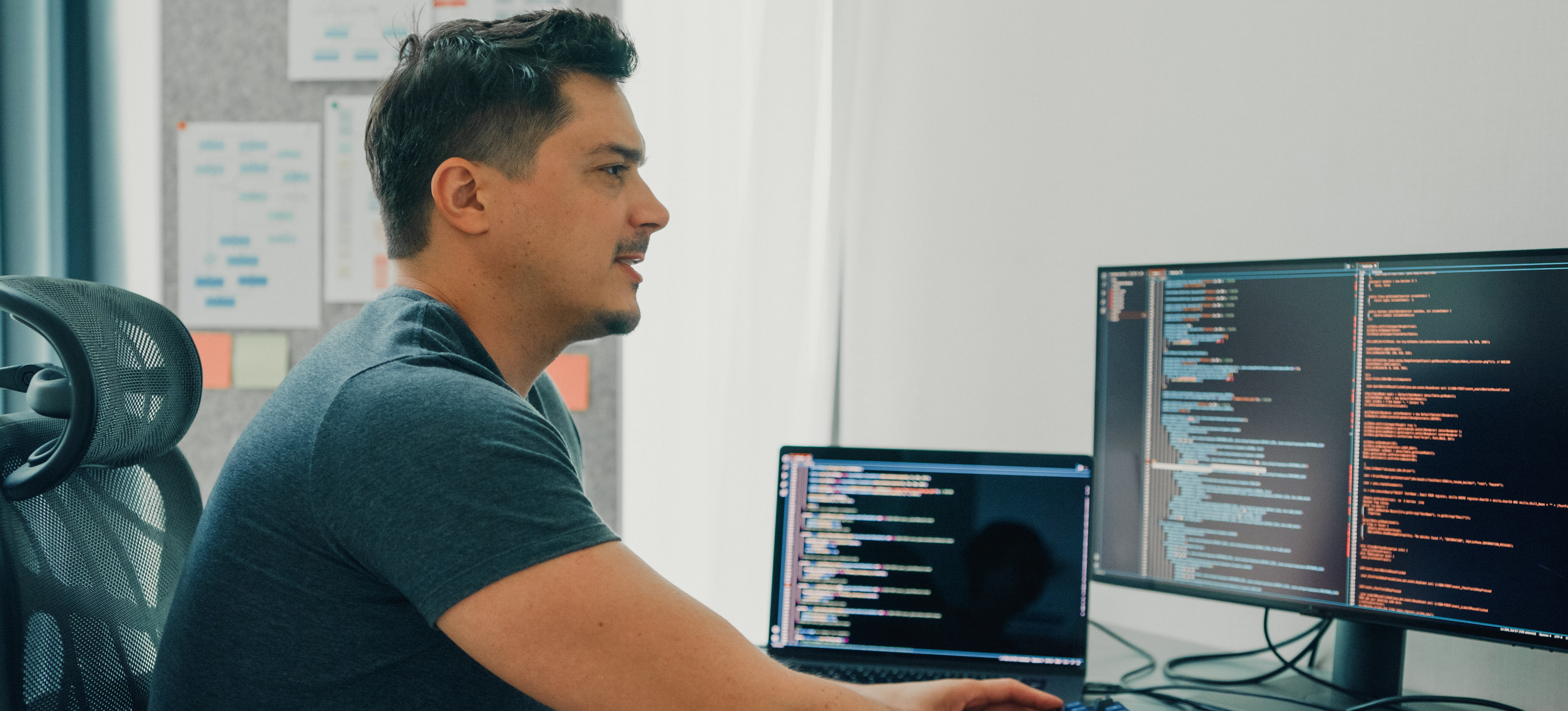[Featured Image] A PHP developer sitting at a desk with multiple screens showing code, learning and improving their PHP programming skills.
