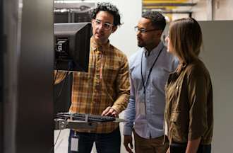 [Featured Image] An embedded systems engineer shows his colleagues a monitor connected to a larger electronic system.