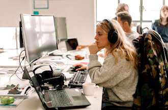 [Featured image] A vigilant woman, wearing a jacket and headphones, closely monitors her computer screen for signs of cyber threats.