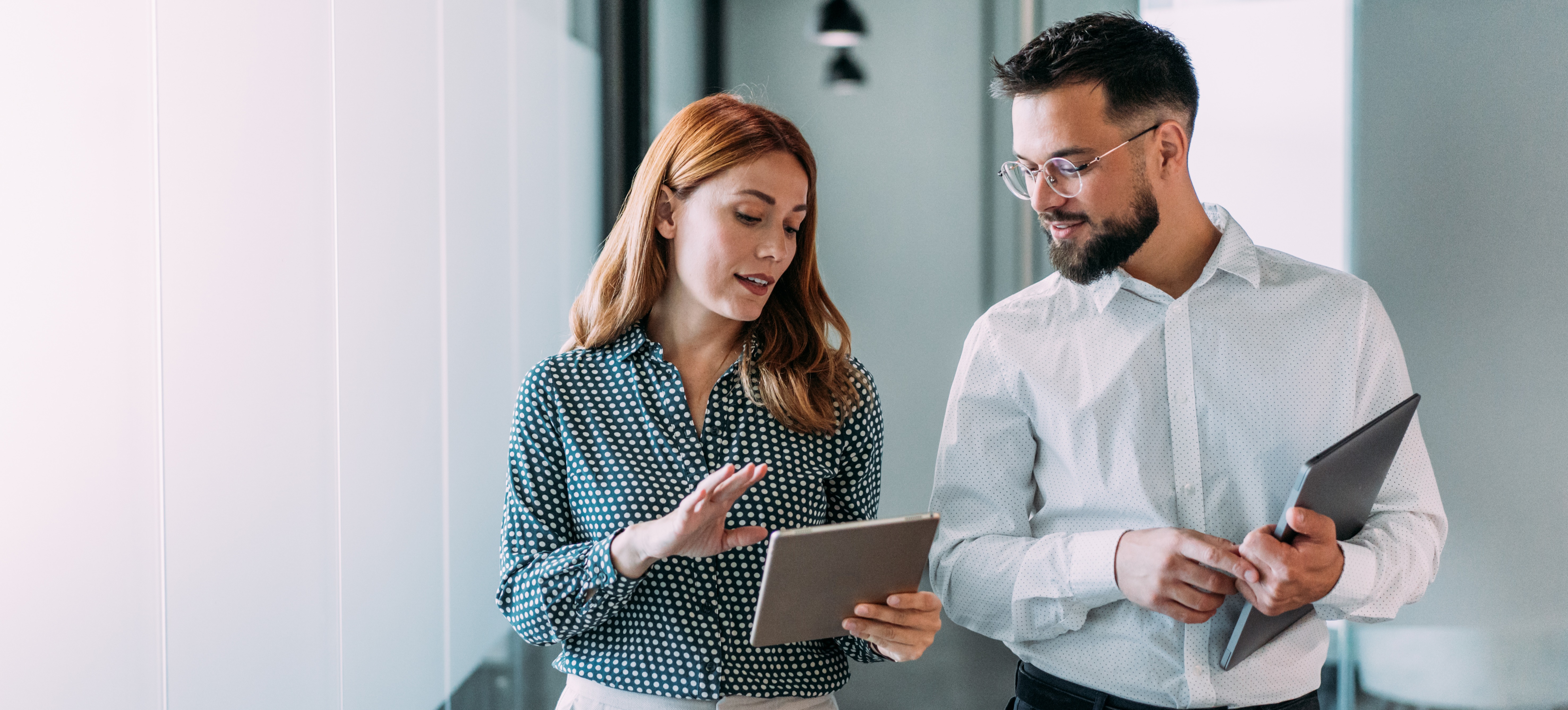[Image en vedette] Un manager marche avec un employé dans un bureau alors qu'ils regardent tous deux une tablette et discutent d'un plan d'amélioration des performances.