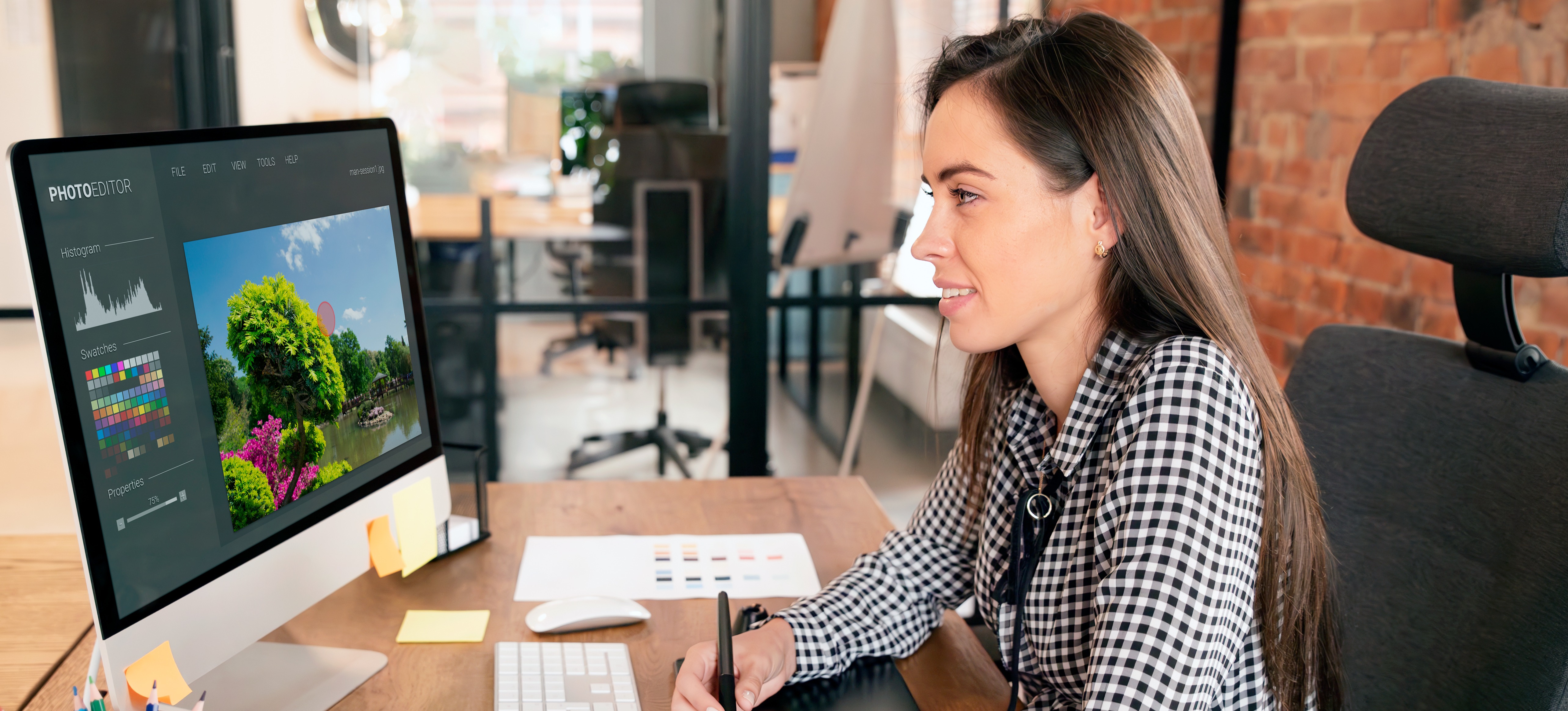 [Featured Image] A visual designer works with a computer and tablet, creating a design project.
