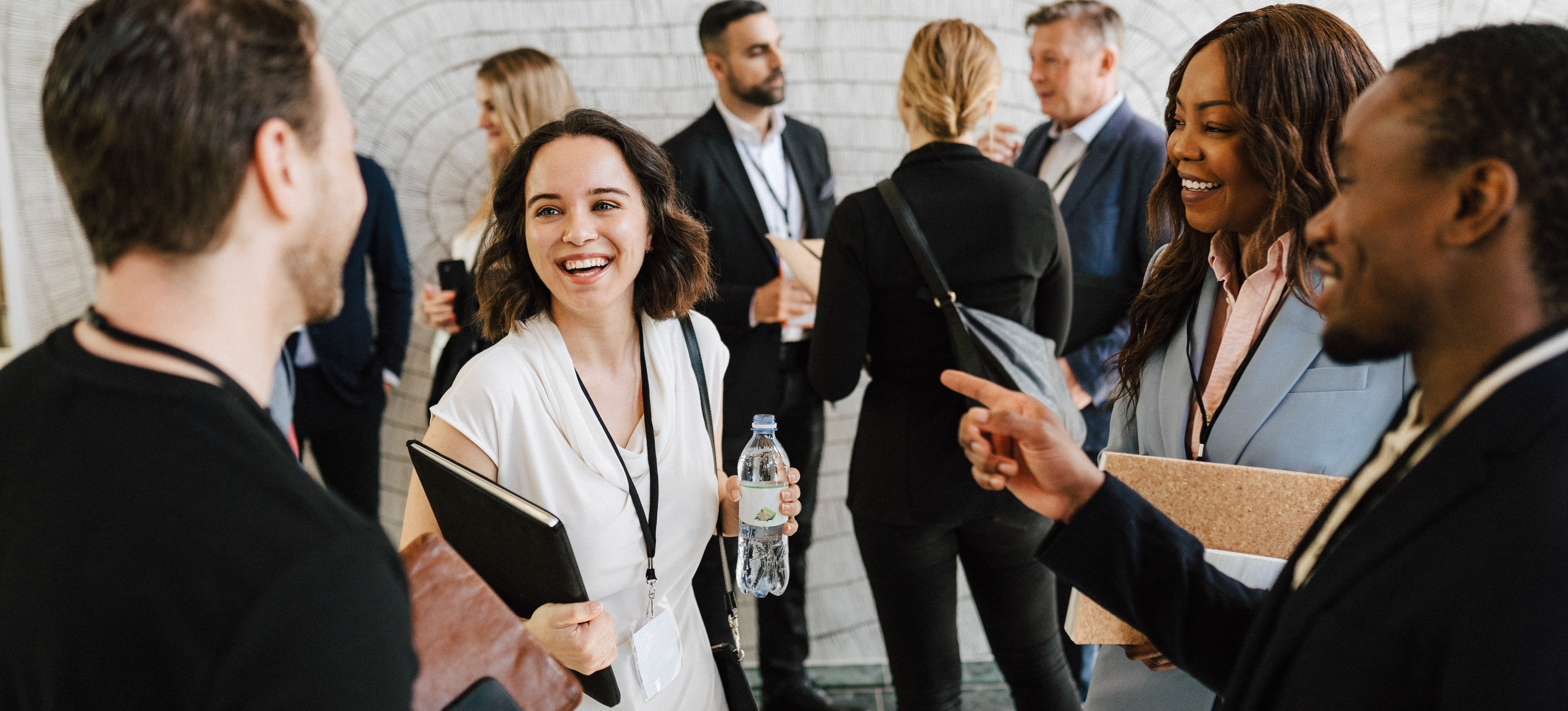 [Featured Image] A group of organizational behavior professionals holding clipboards and wearing lanyards gather together at a conference. 
