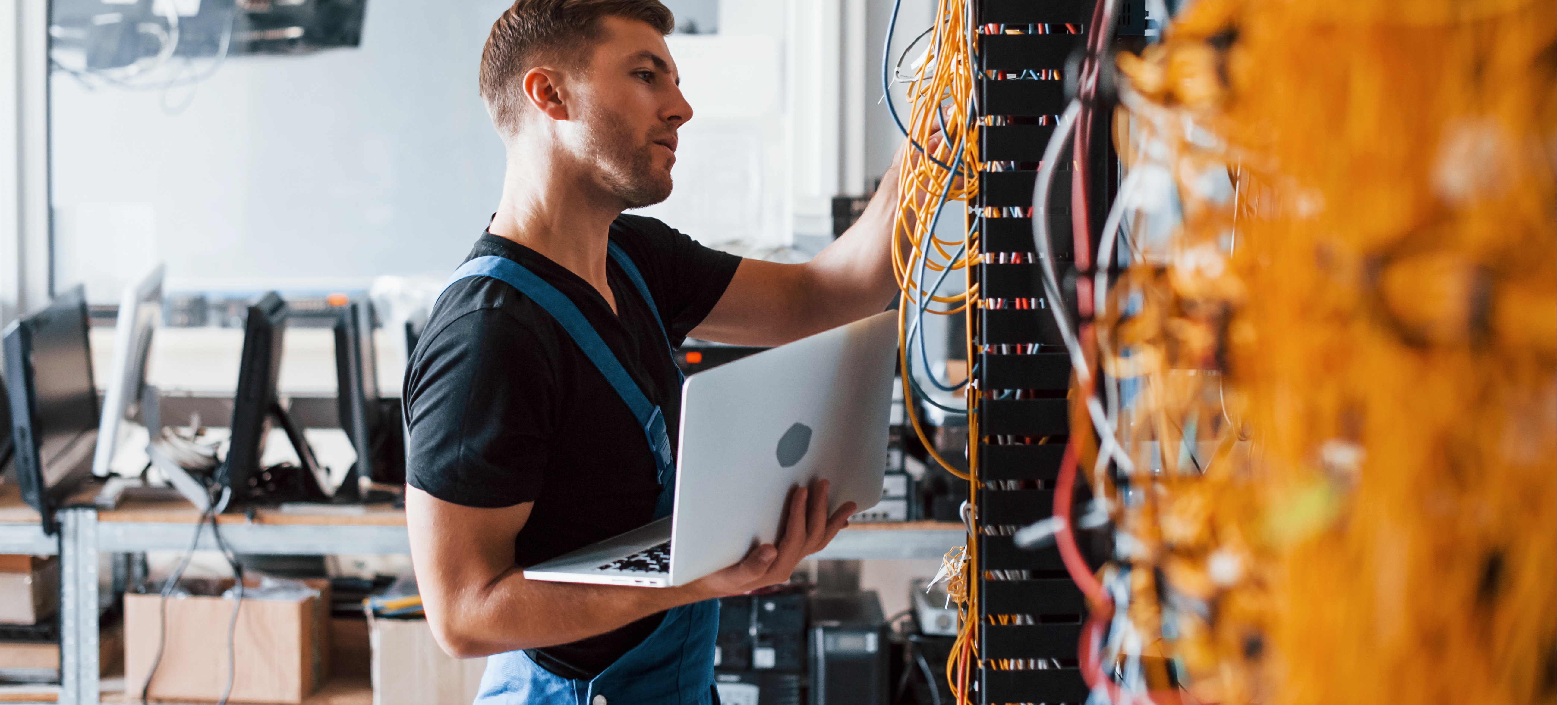 [Image en vedette] Un jeune administrateur de système en uniforme de travail travaille sur les câbles d'un serveur pour s'assurer qu'il fonctionne correctement.