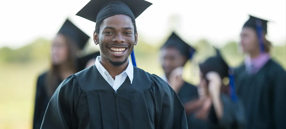[Featured image] A finance major wearing a cap and gown stands outside after a graduation ceremony, holding their degree.