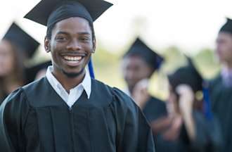 [Featured image] A finance major wearing a cap and gown stands outside after a graduation ceremony holding his degree.