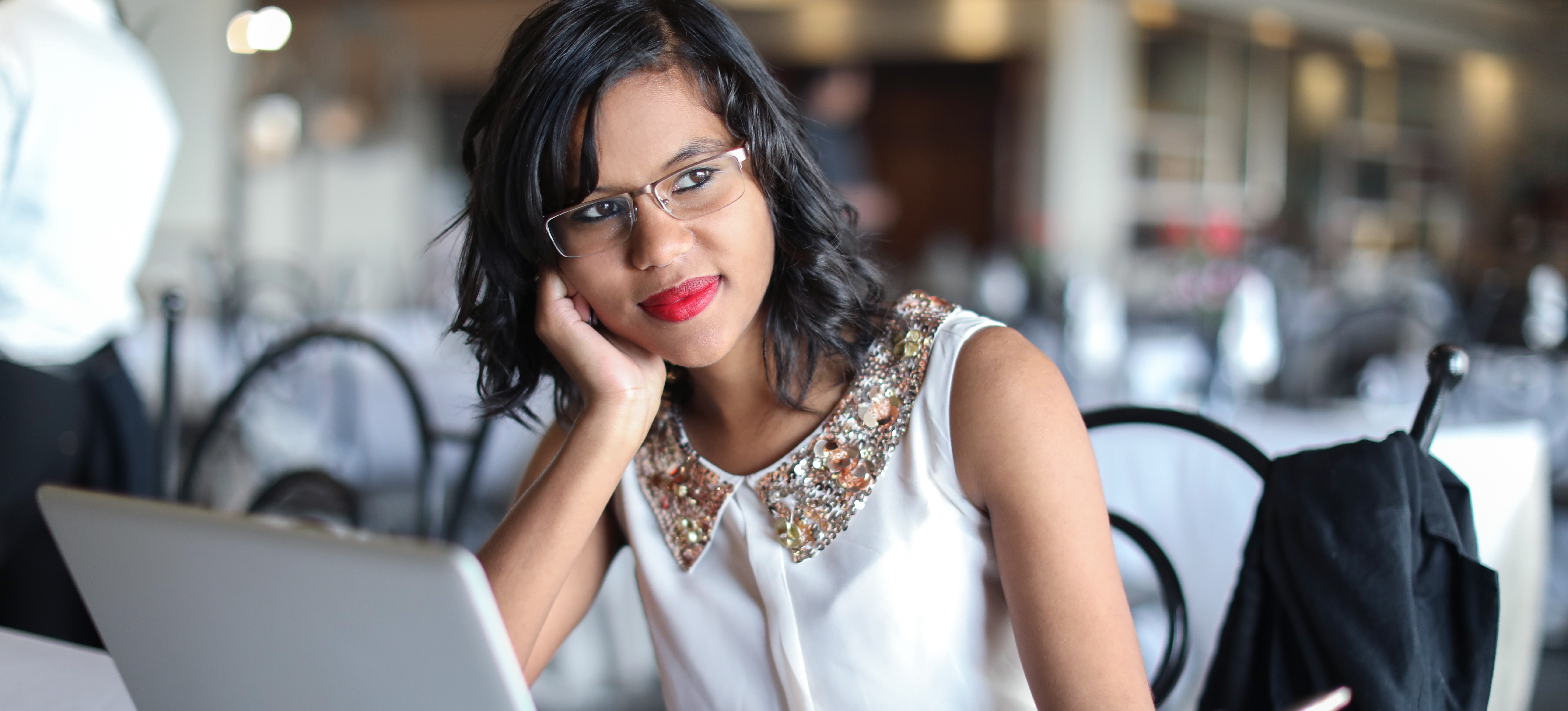 [Featured Image] A woman sits at a laptop in a cafe and contemplates earning her Post Graduate Diploma in Management (PGDM) upon learning about the potential PGDM salary.
