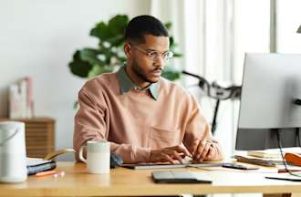 [Featured Image] A system administrator is in front of their computer on their desk, researching new jobs and system administrator salaries.