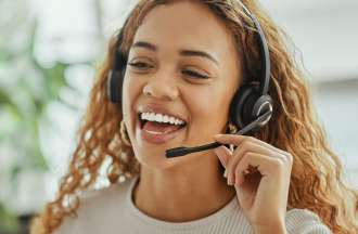 [Featured Image] A smiling customer service representative wearing a headset speaks to a customer on the phone when ChatGPT is not able to answer their questions.
