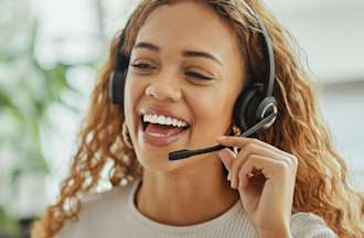 [Featured Image] A smiling customer service representative wearing a headset speaks to a customer on the phone when ChatGPT is not able to answer their questions.
