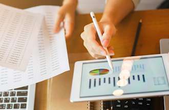 [Featured Image] Two workers look at a business intelligence dashboard on their tablet and computer.