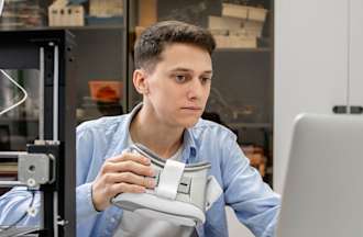 [Featured image] A data science student in a blue shirt and holding goggles works on his computer.