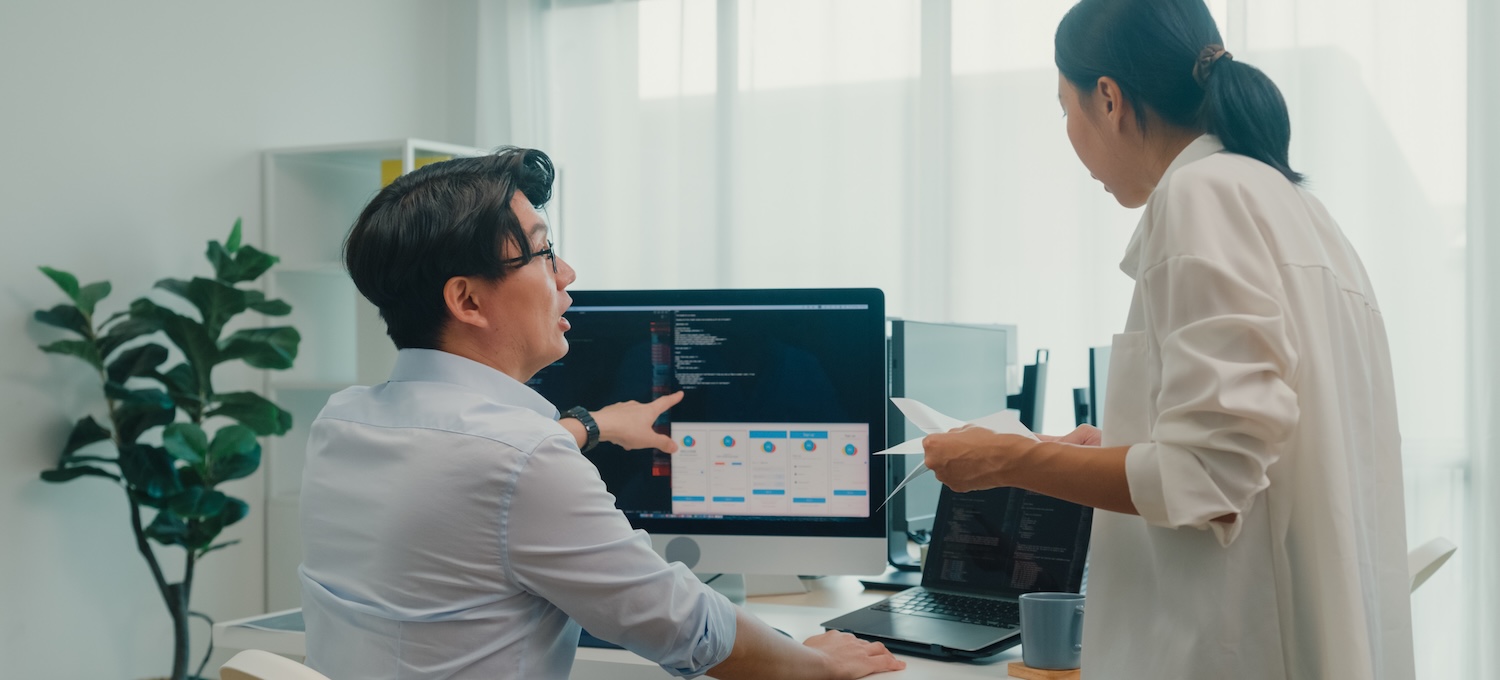 [FEATURED IMAGE] Two data science professionals perform their data science jobs, looking at a desktop computer in an office.
