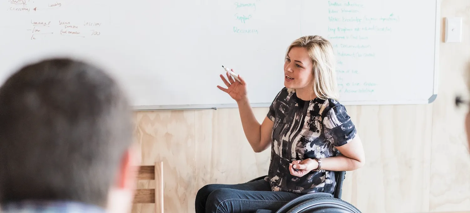 [Featured image] A person in a wheelchair draws elements of a user journey map for a team of colleagues