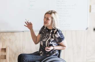 [Featured image] A person in a wheelchair draws elements of a user journey map for a team of colleagues
