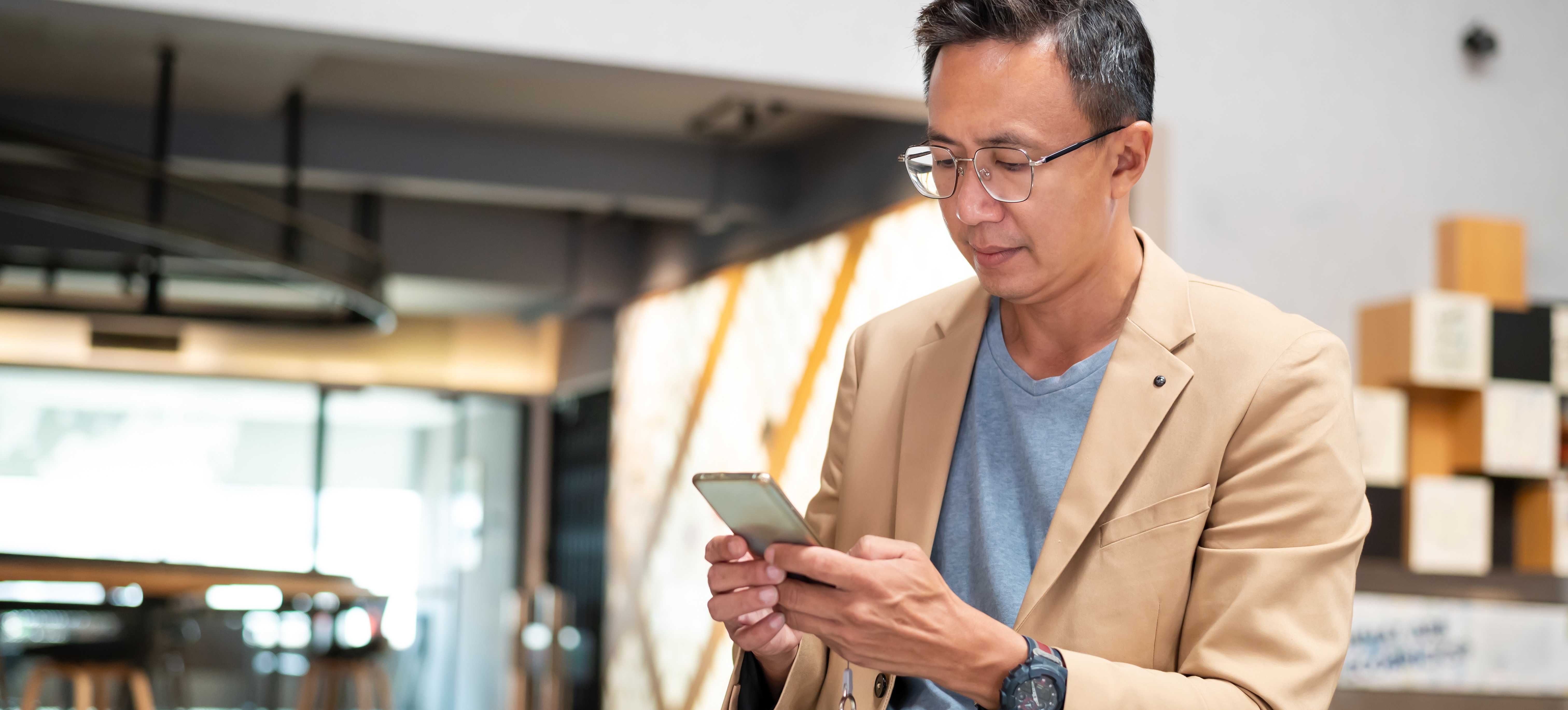 [Hauptbild] Ein Geschäftsmann in einem beigen Blazer und einem grauen Hemd sieht sich ganz entspannt auf seinem Smartphone Informationen zum mobilen Lernen an und freut sich über eine neue Möglichkeit zur beruflichen Weiterentwicklung.
