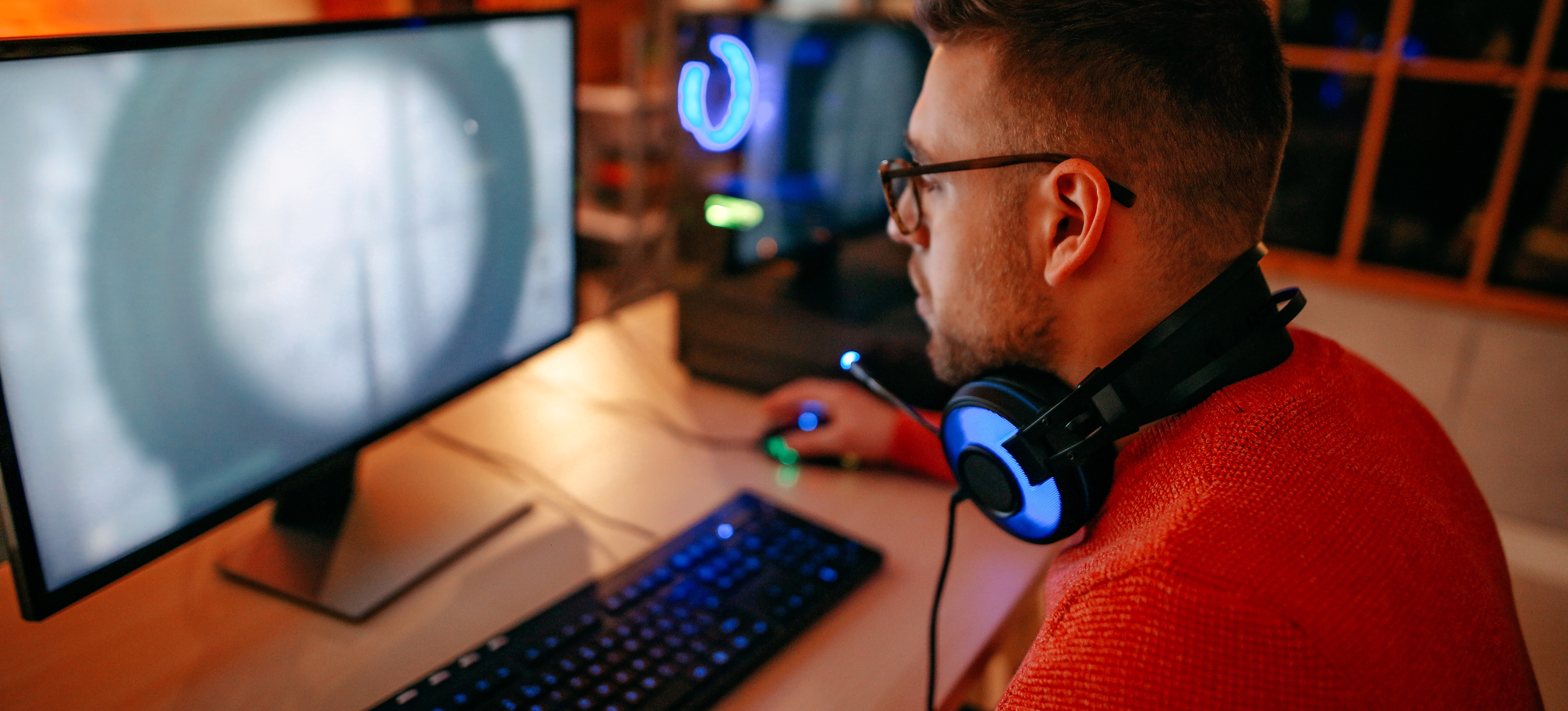 [Featured image]: A person wearing headphones around their neck works at a computer after discovering how to learn Python for game development.