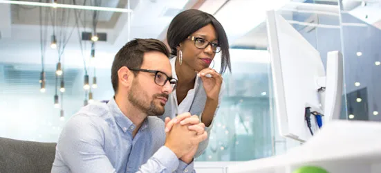 [Featured Image] Two data scientists look at a computer screen in their office and discuss Spark versus MapReduce.
