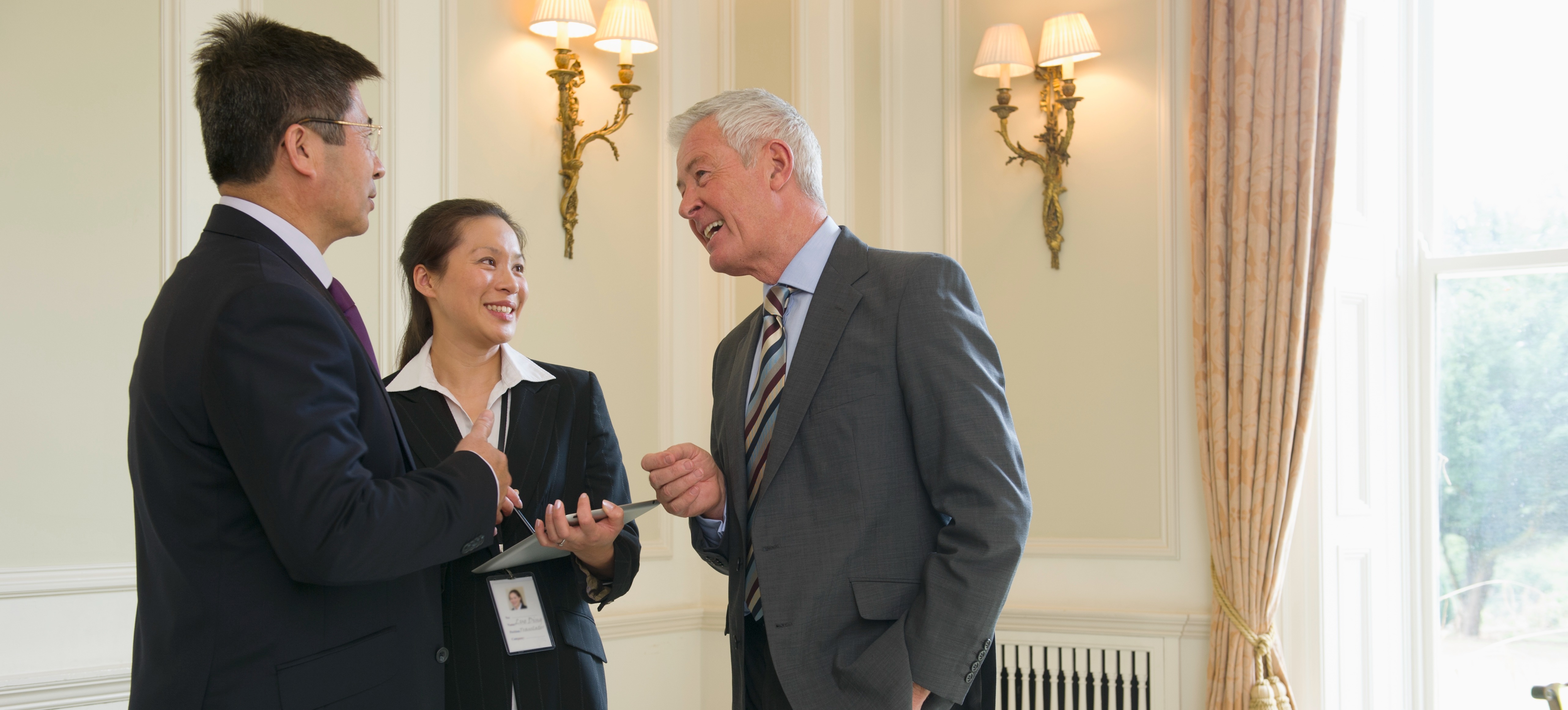 [Featured Image] Three government workers talking in a federal office.
