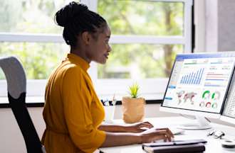 [Featured image] Woman in yellow dual-screen reviewing data analysis

