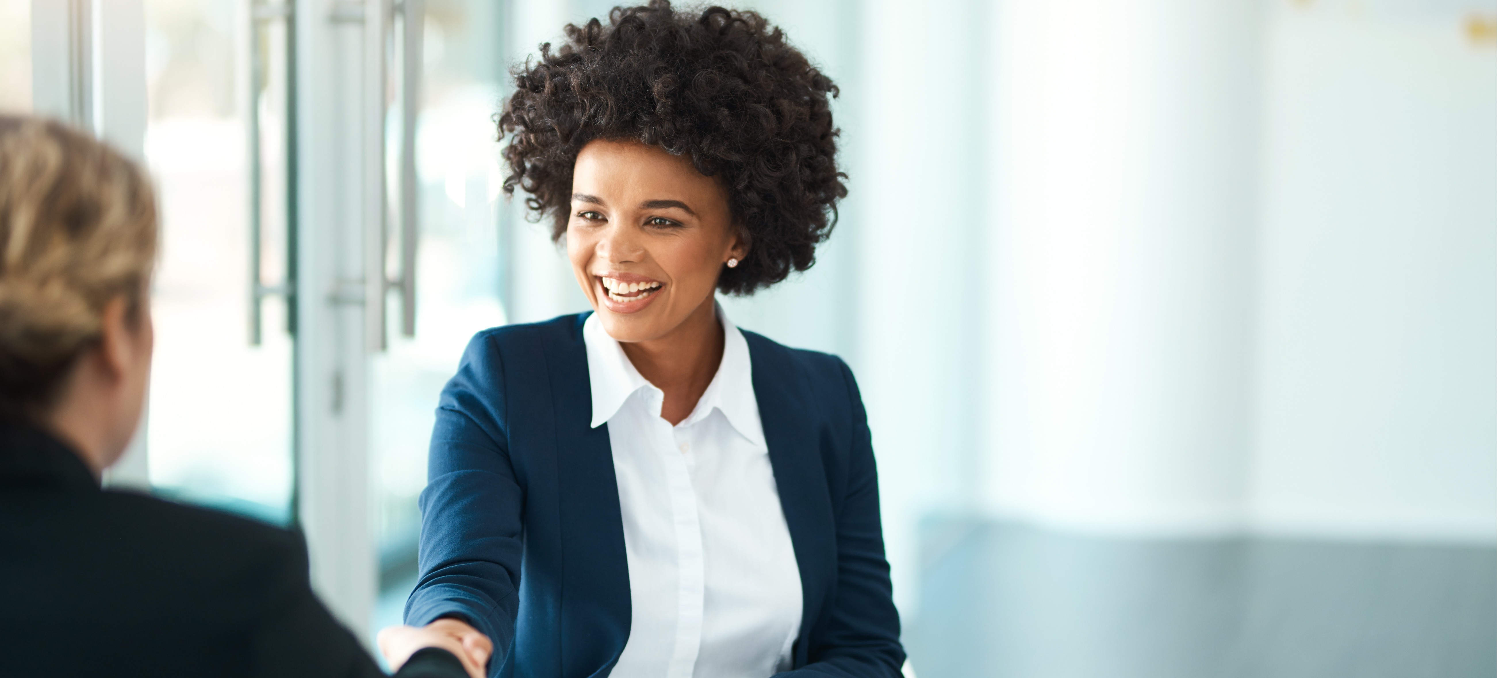 [Featured Image] A young female AI professional sitting at a white table in an office having an interview with deep learning interview questions and shaking the hand of the person interviewing her.
