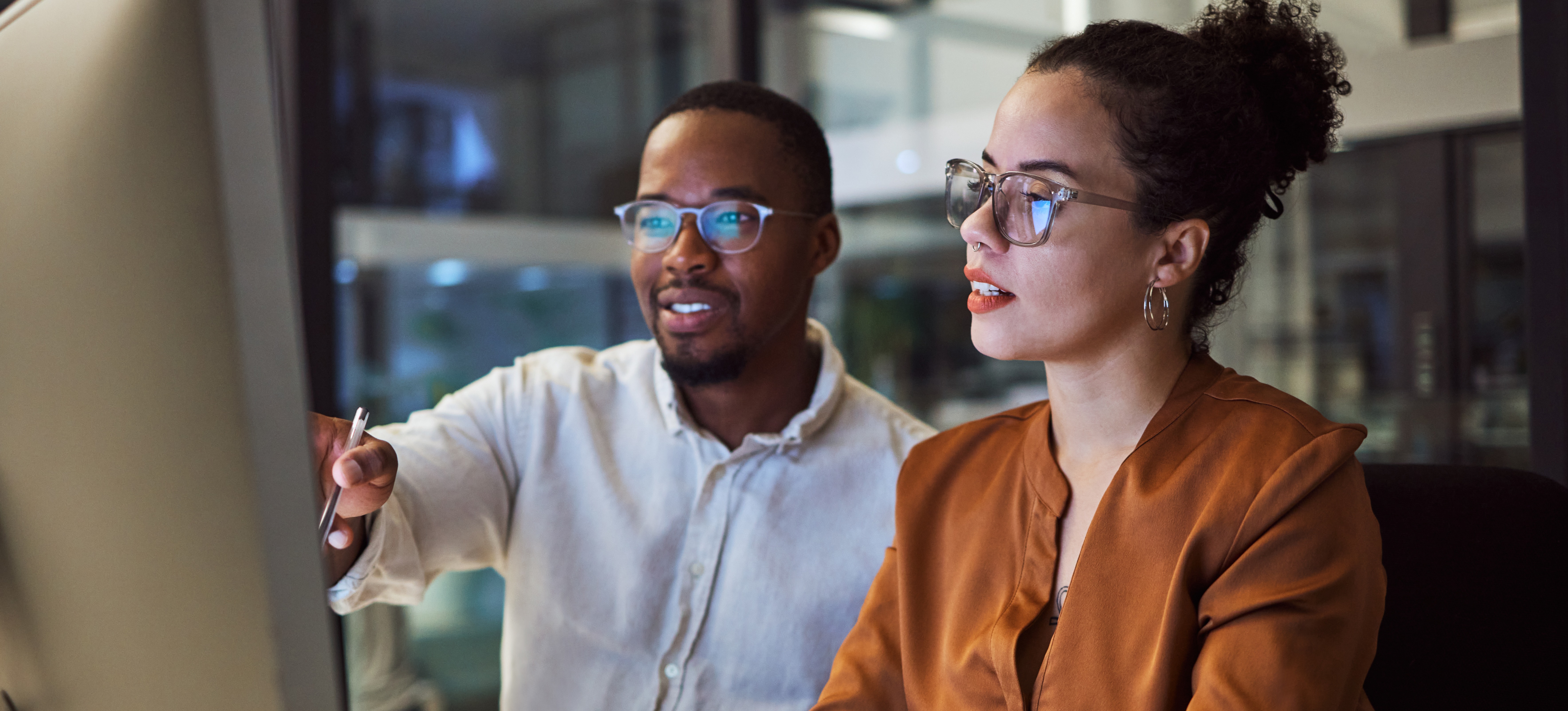 [Featured Image] A trainer sits with a new employee during the onboarding process and explains a procedure as they both look at a computer screen, and the new employee types on the keyboard.
