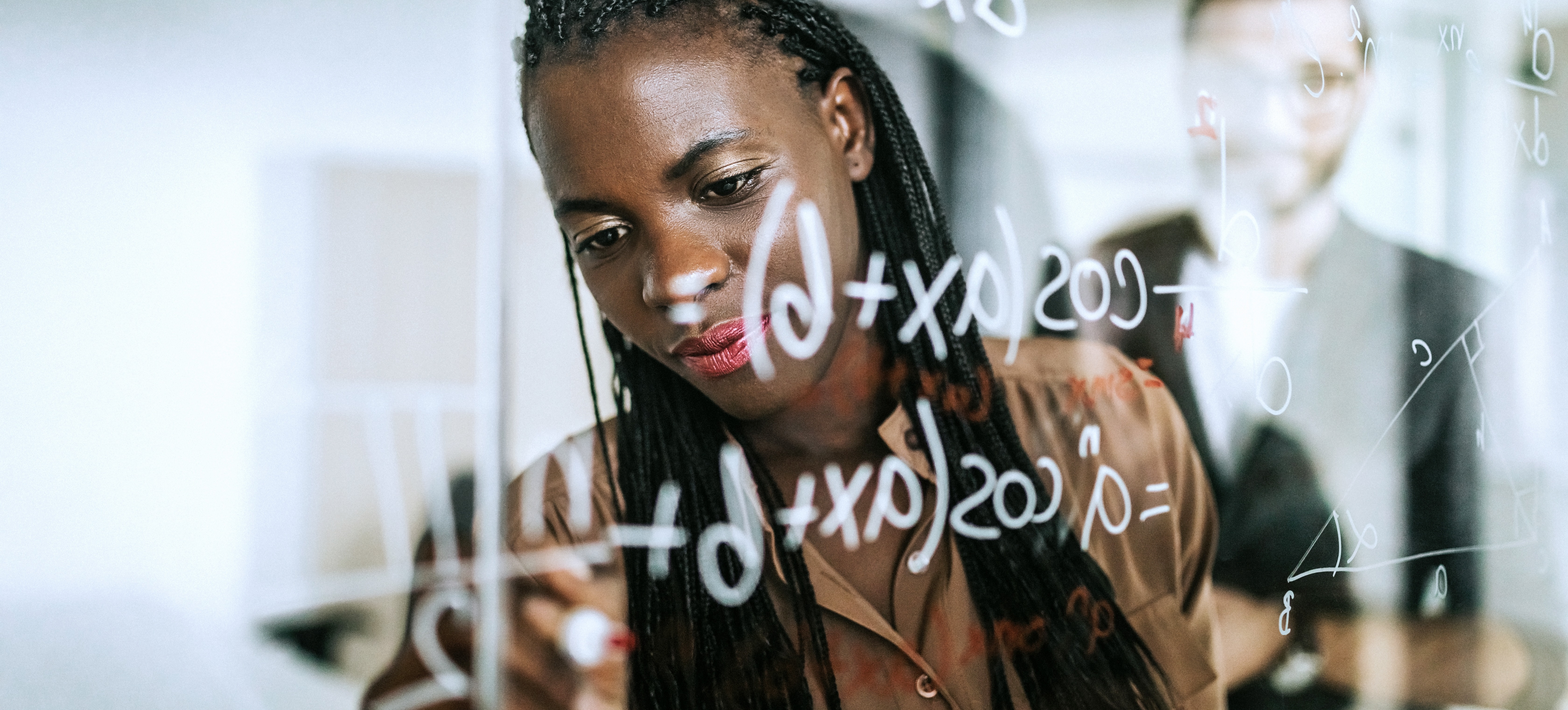 [Featured Image] A woman professional exhibits one of the many math careers available, while writing a mathematical equation on a transparent wipe board.
