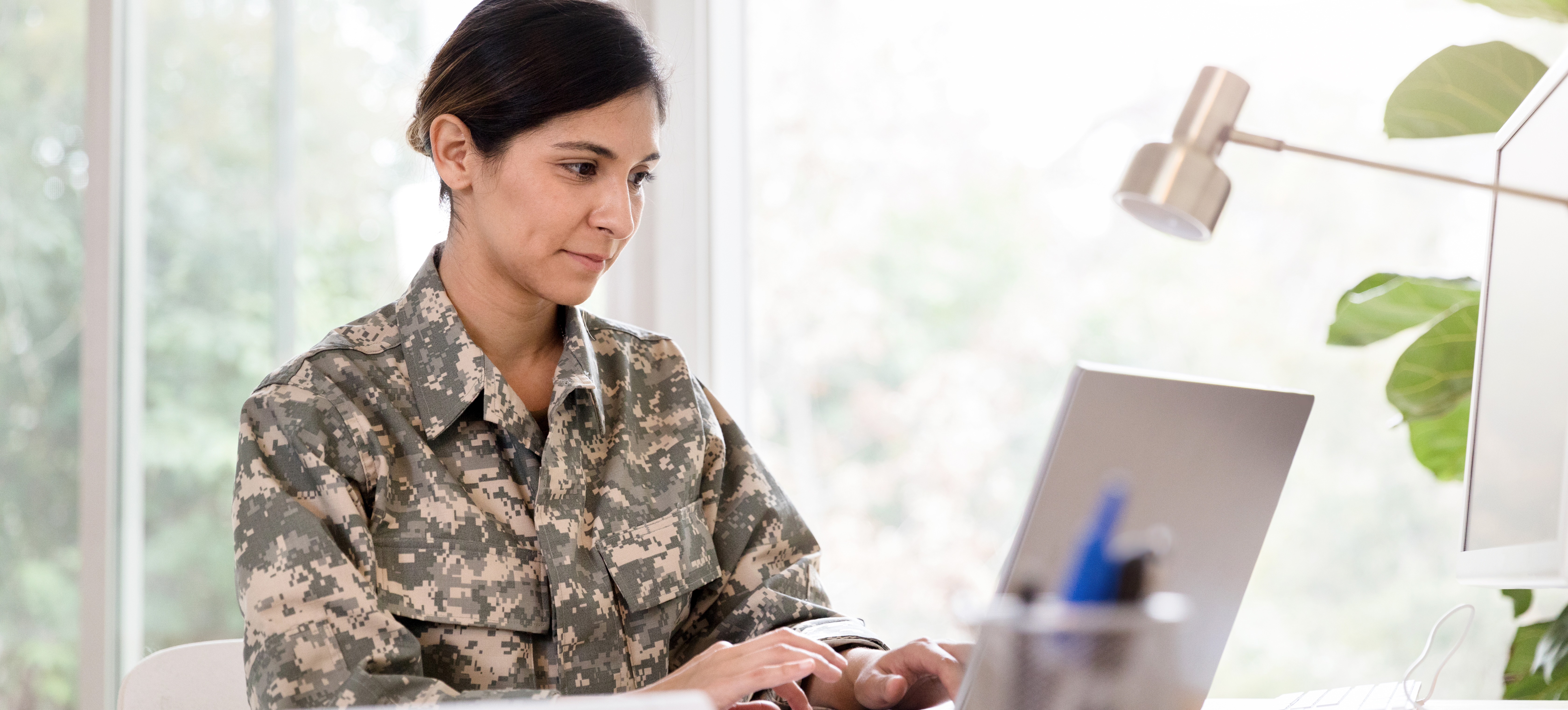 [Featured Image] A soldier wearing camouflage sits at a desk and uses a laptop to research jobs for veterans.
