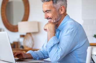 [Featured Image] A man sits at his laptop at home and prepares to earn a certification to become an AWS Certified Solutions Architect. 
