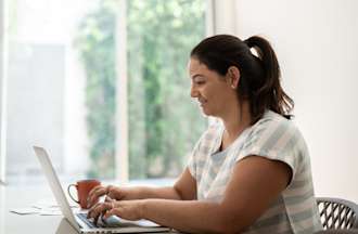 [Featured Image] A woman who wants to make a career change uses her laptop at home to research the potential Power BI developer salary and job outlook. 
