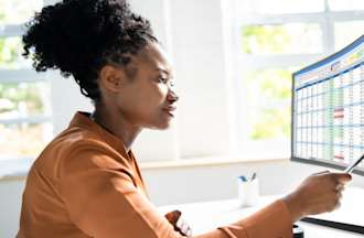 [Featured Image] Woman in a rust-colored long-sleeved shirt looking at computer screens displaying business intelligence data for risk assessment.
