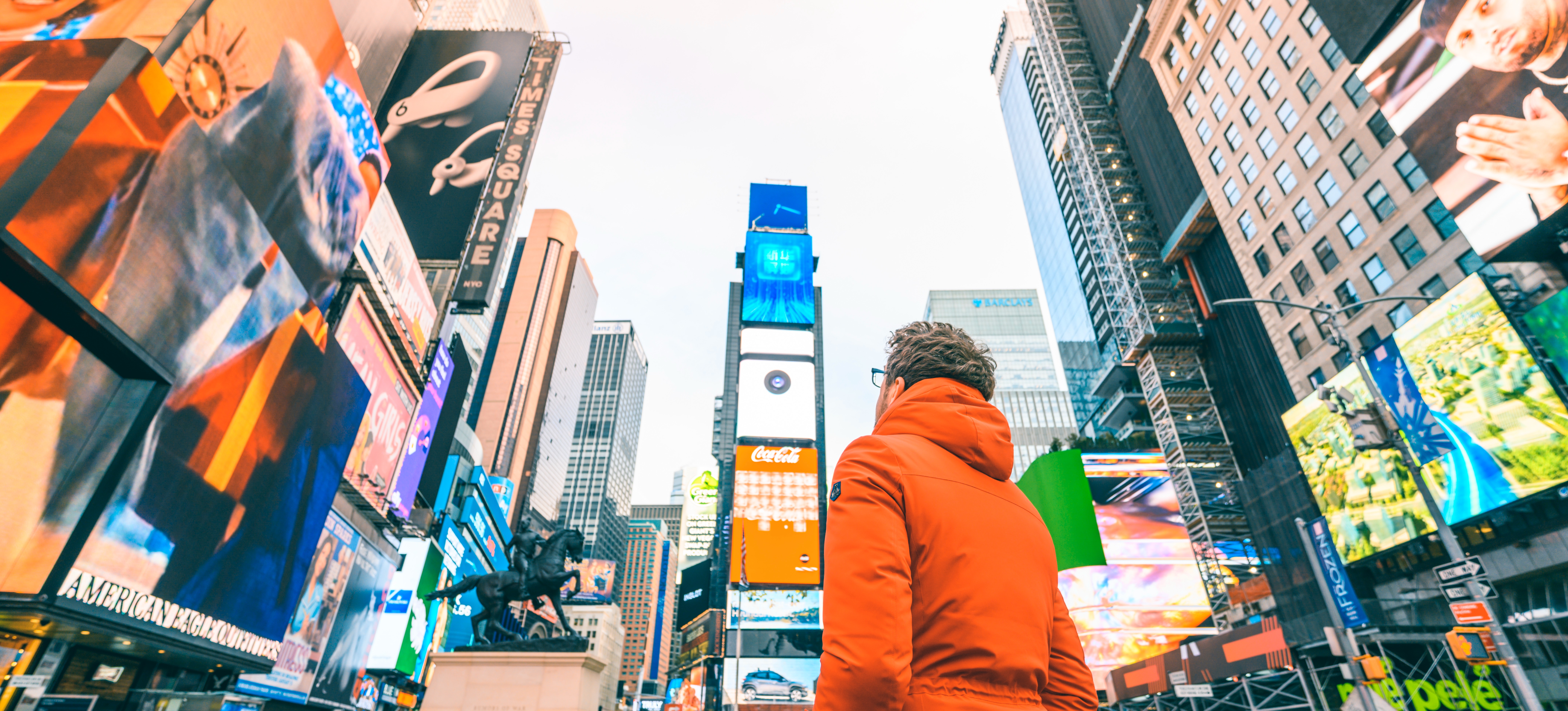[Featured image] A person in an orange parka stands in Times Square looking up an example of guerrilla marketing advertisement.