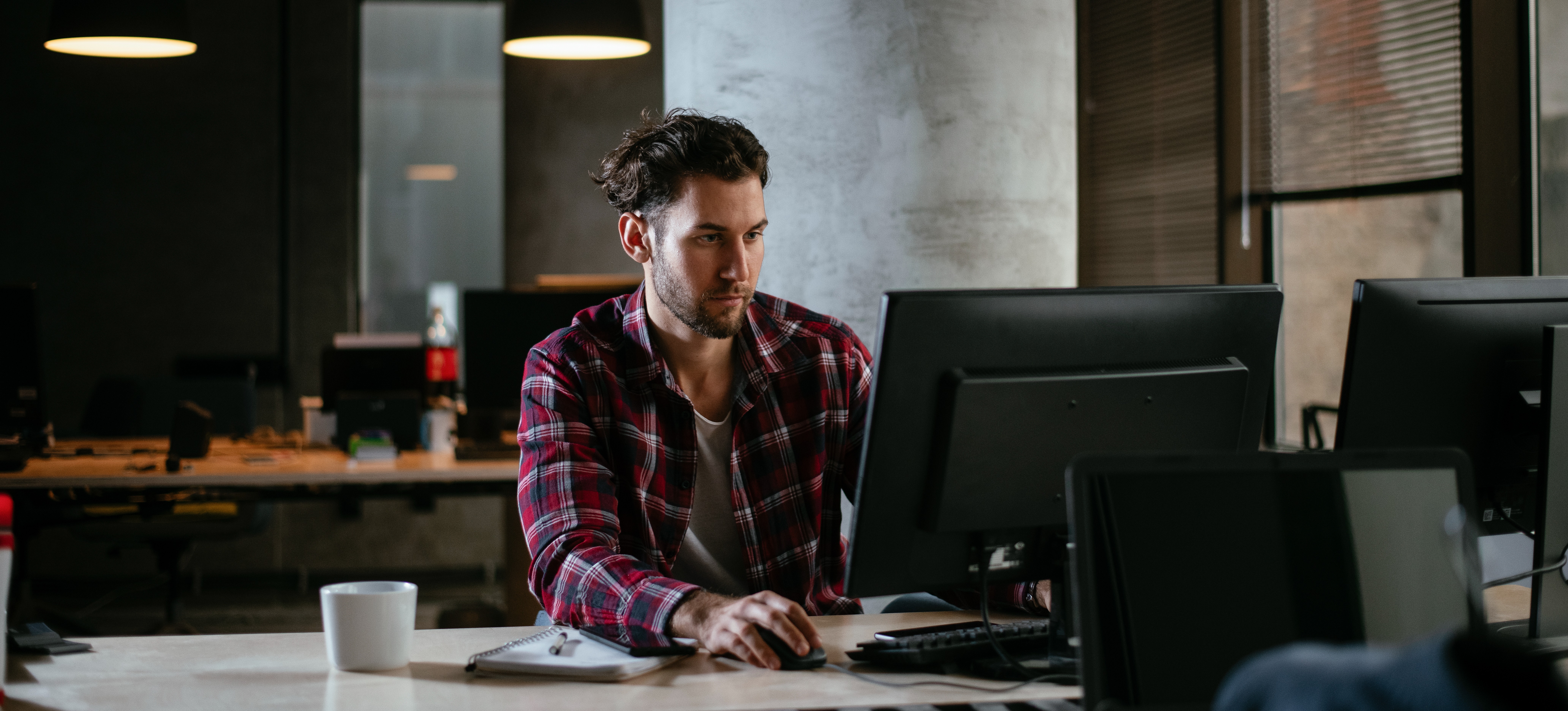 [Featured Image] A red hat certified systems administrator who earns an RHCSA salary works at their computer in an office space in the evening.
