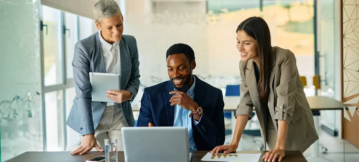 [Featured Image]: Three professionals stand around a laptop, applying critical thinking skills to work through a challenge with ChatGPT.
