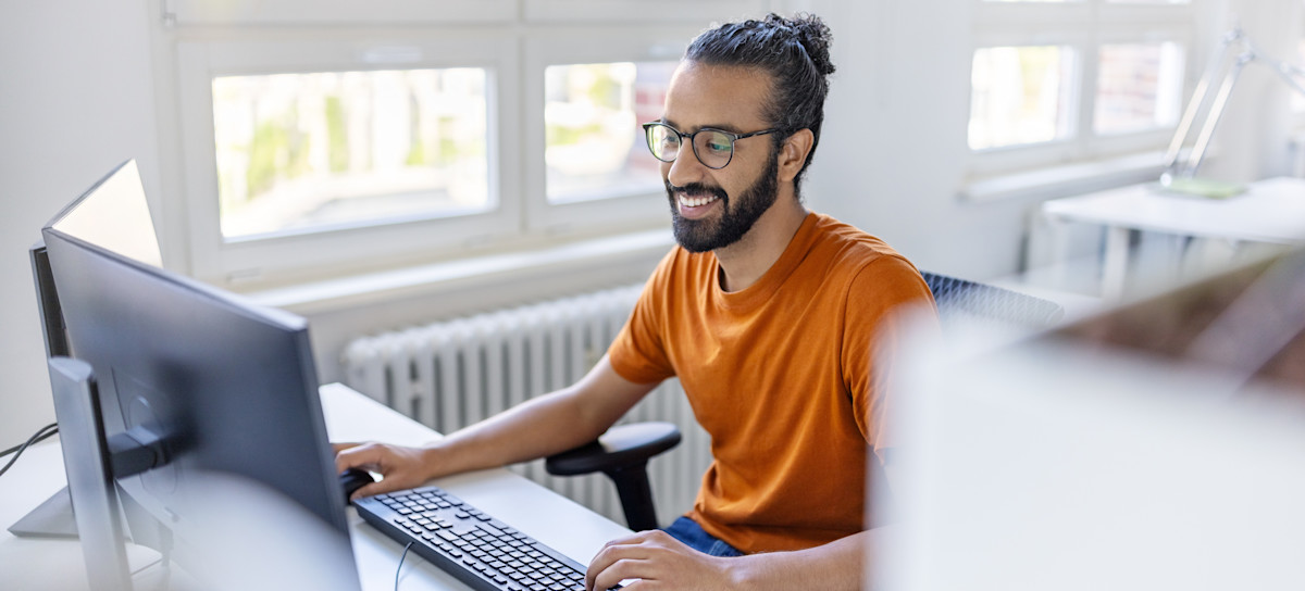 [Featured Image] A software engineering professional sits at a desktop computer and performs an entry-level software engineering job.
