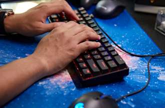 [Featured Image] Two hands hover over a colorful light-up keyboard sitting on a galaxy-printed desk mat next to a computer mouse.