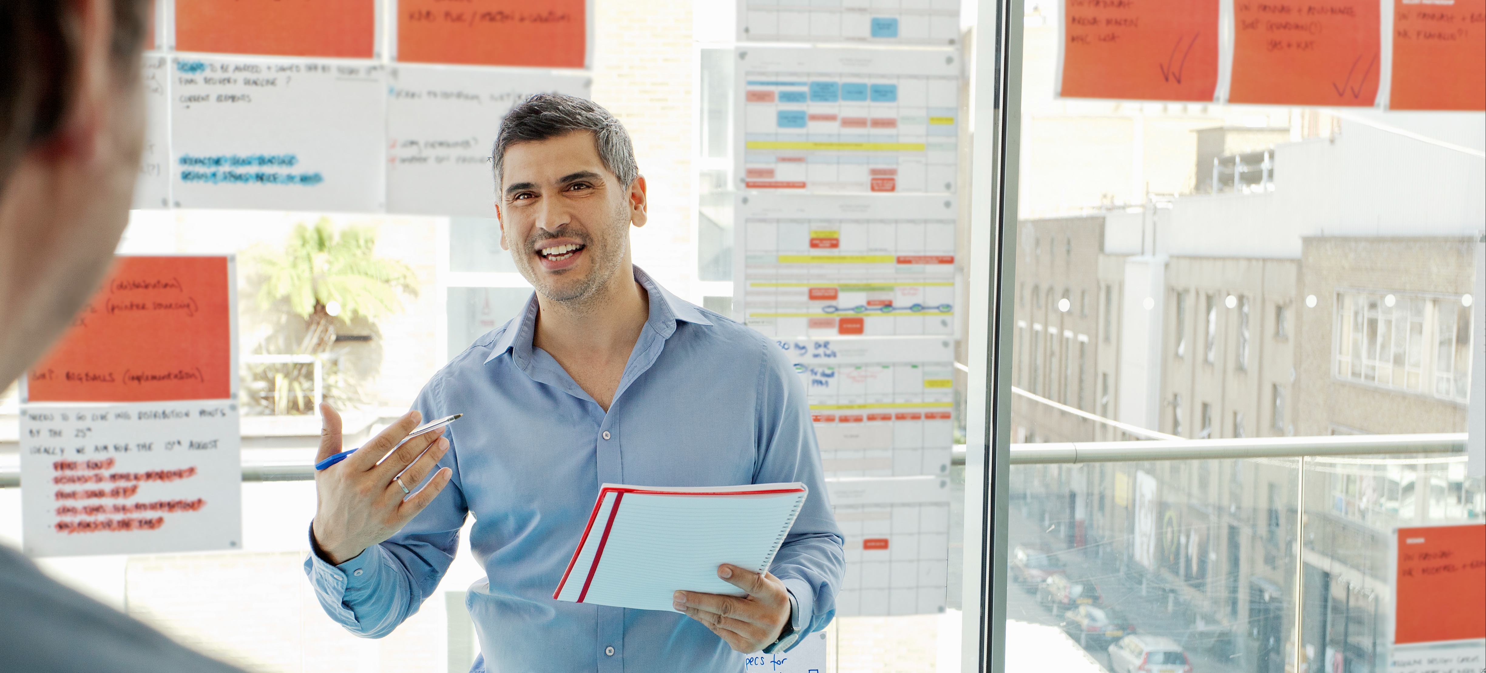 [Featured Image] A project manager stands in front of multicolored charts and discusses Gantt charts with colleagues.