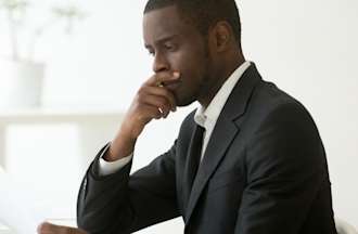 [Featured Image] Serious African-American professional using analytical thinking as he reads a document at his workspace.
