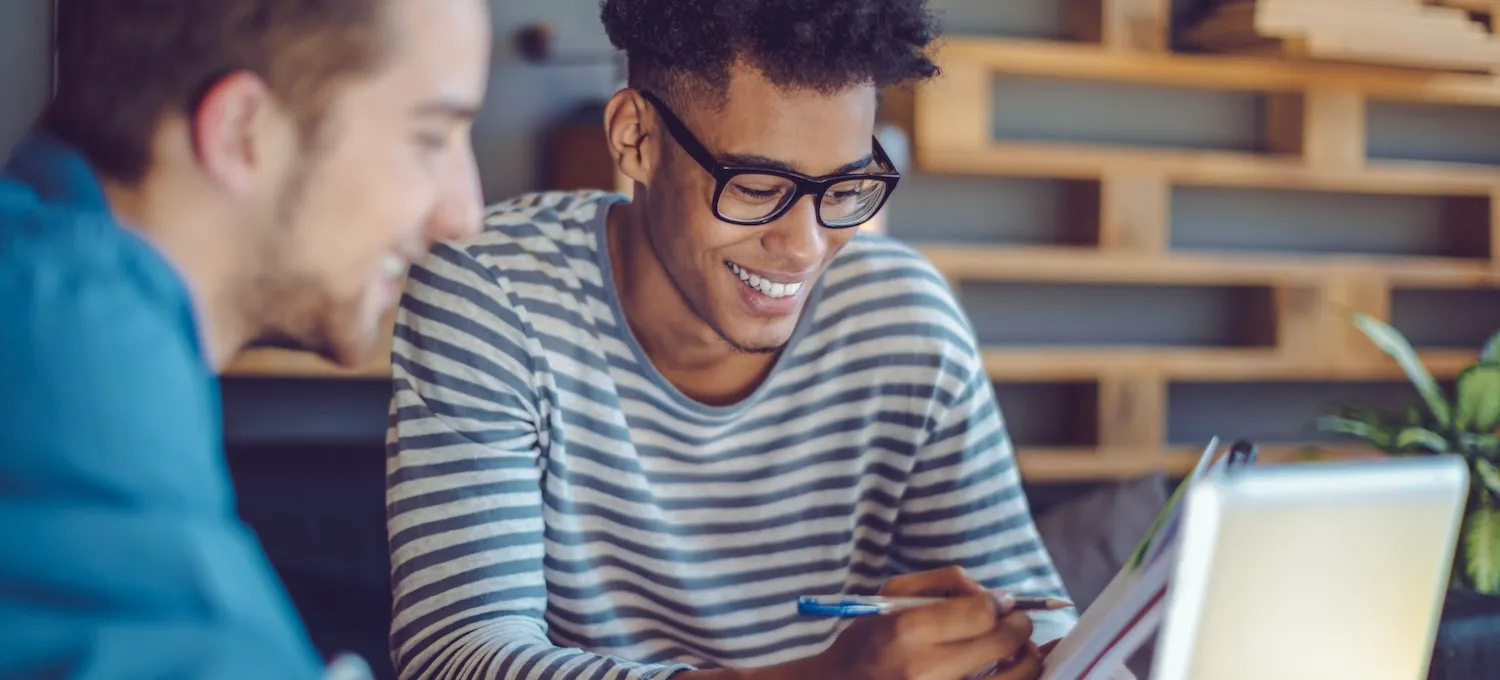 [Featured image] Two friends sit around a laptop discussing reasons to go to college.