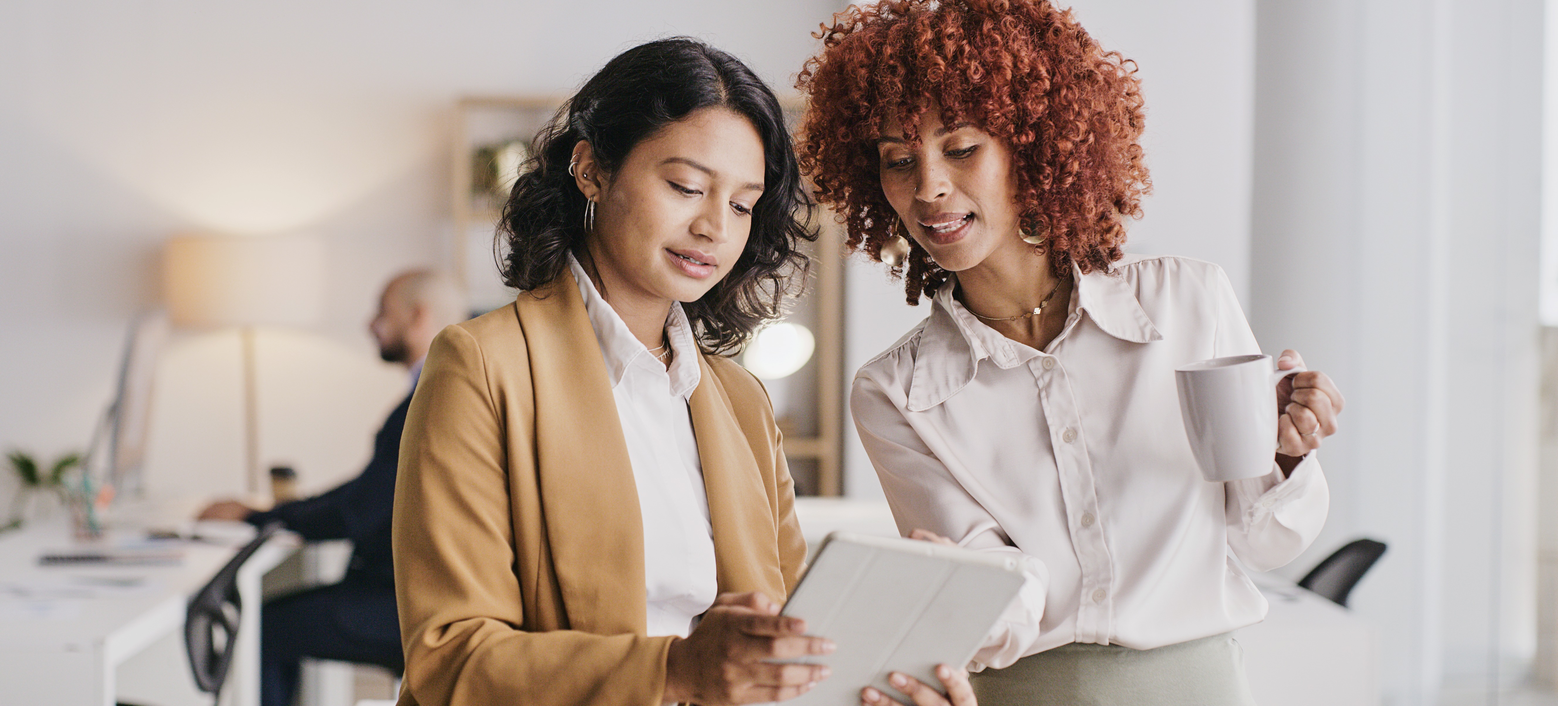 [Featured Image] A woman with a software sales salary shows a client something on a tablet in an office setting.
