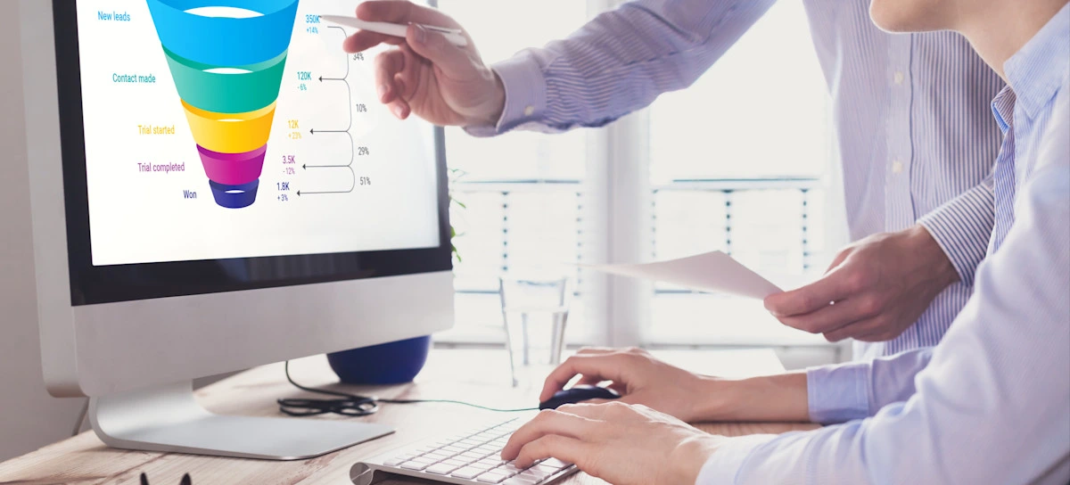 [Featured Image] A sales operations analyst explains their findings using a visual of the sales funnel to help their colleague understand the implications. 
