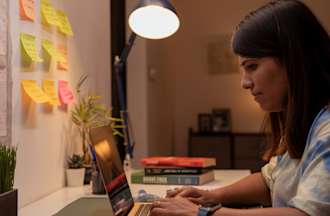 [Featured Image] A graduate student earning a master's in IT management is studying at her desk and looking at her computer. 