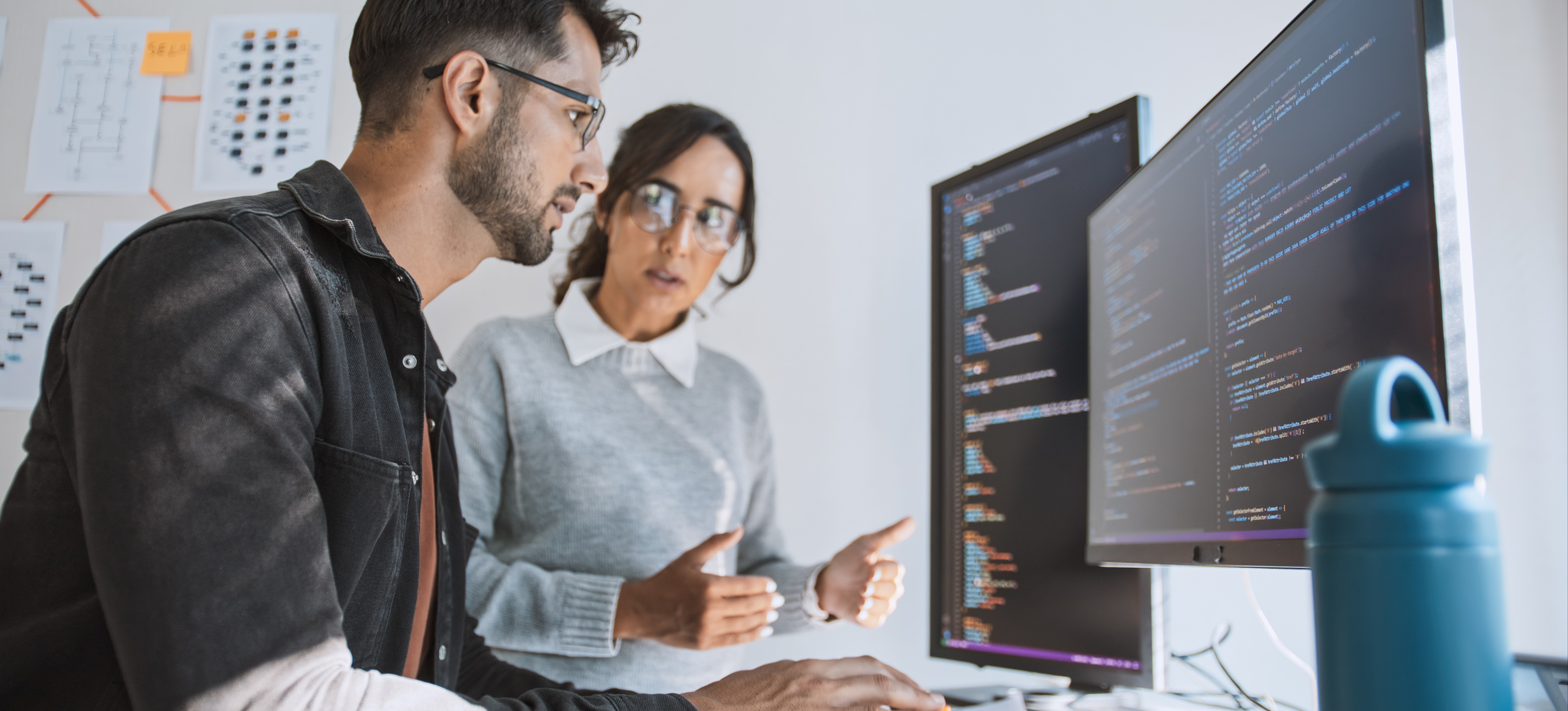 [Featured Image] Two coding engineers implement AI into their software development process.
