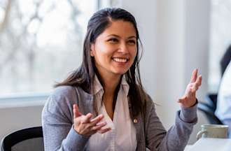 [Featured image] A young woman working in healthcare administration speaking animatedly with her colleague.