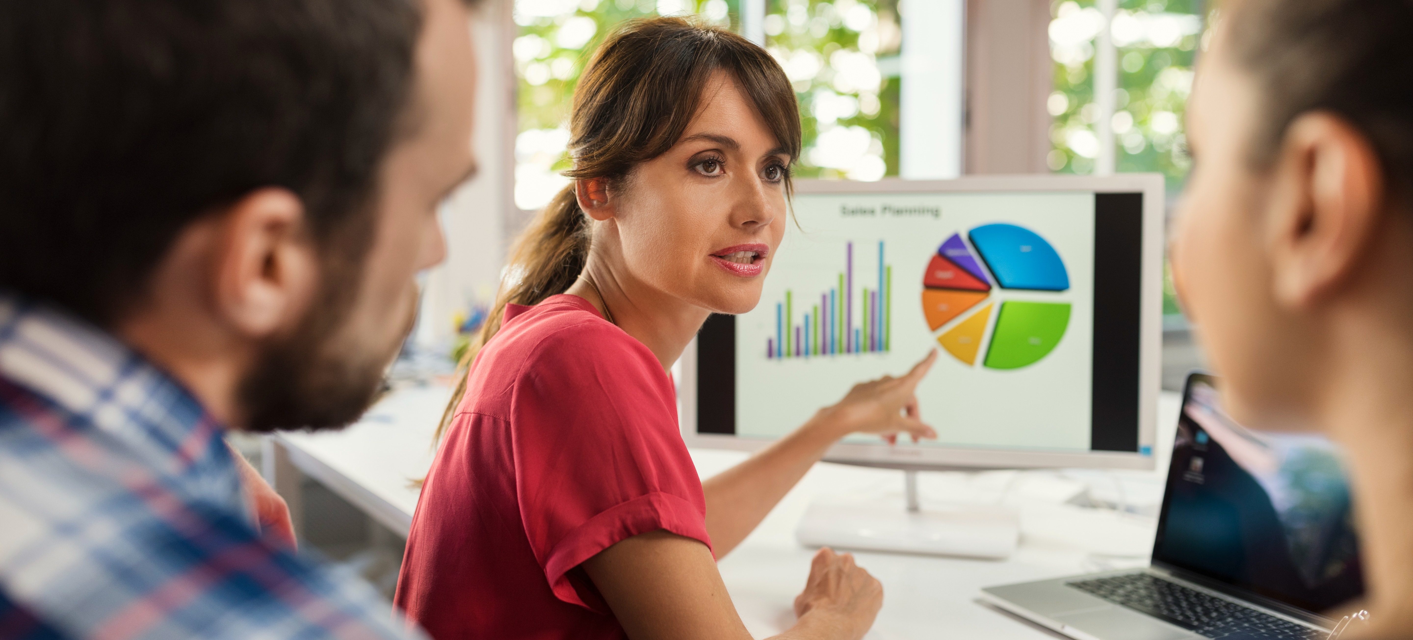 [Featured Image] A team sits around a computer, using a database schema to help organize and represent data.
