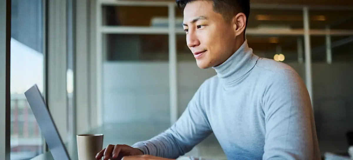 [Featured Image] A smiling person uses ChatGPT agent on a laptop in a sunny office space.

